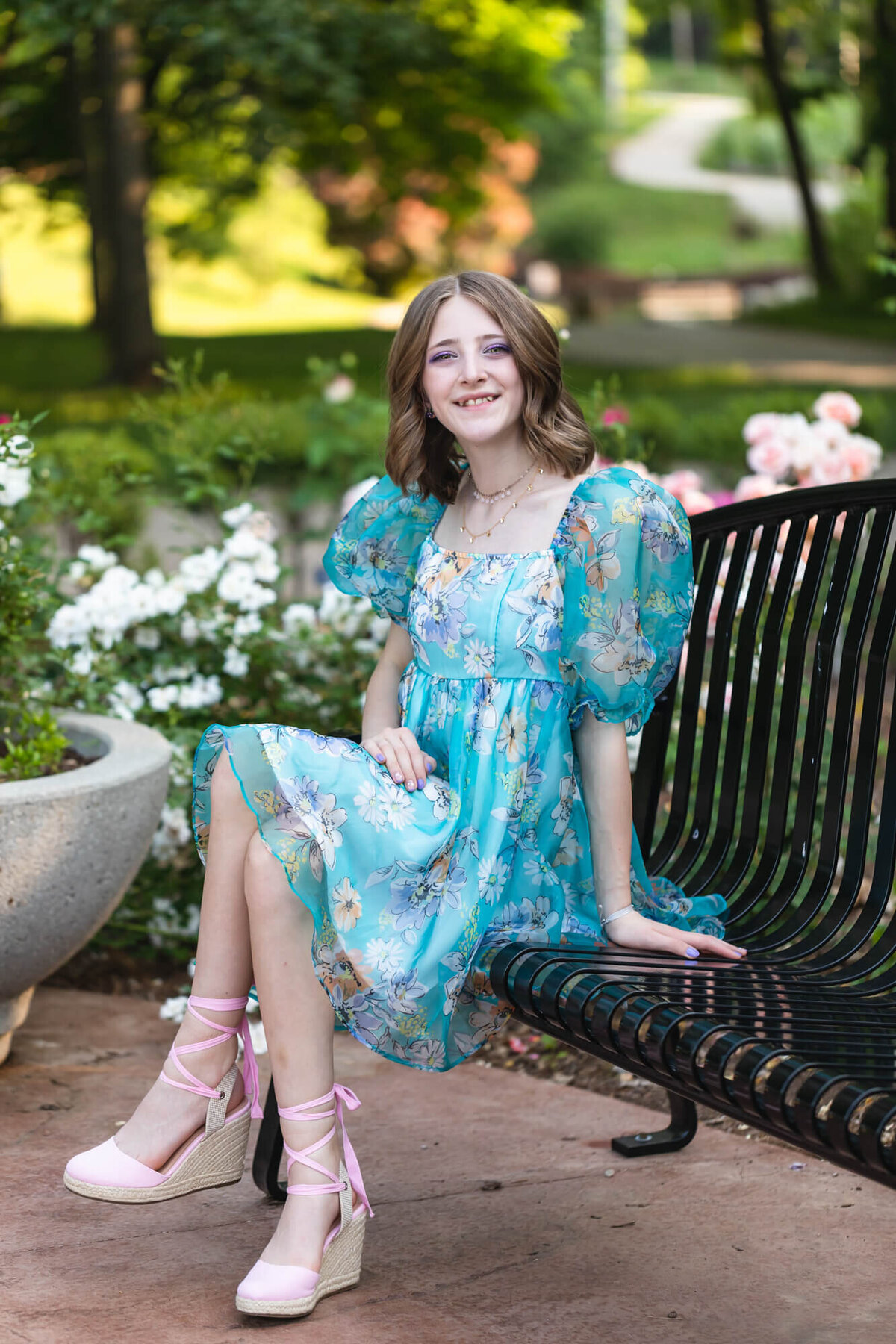 A pretty young teen girl wearing a floral blue puffed sleeve dress with pink wedge shoes at the Springfield Botanical Gardens in the Spring. Captured by Springfield, MO teen photographer Dynae Levingston.