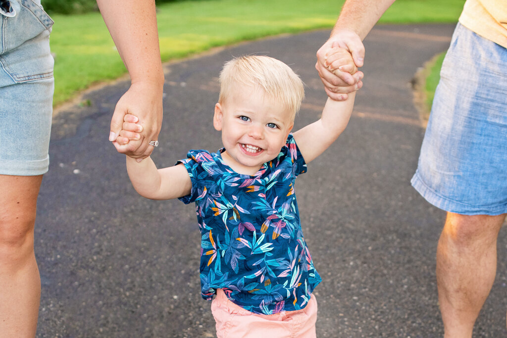 Happy boy holds parents hands on path at Fort Island Park