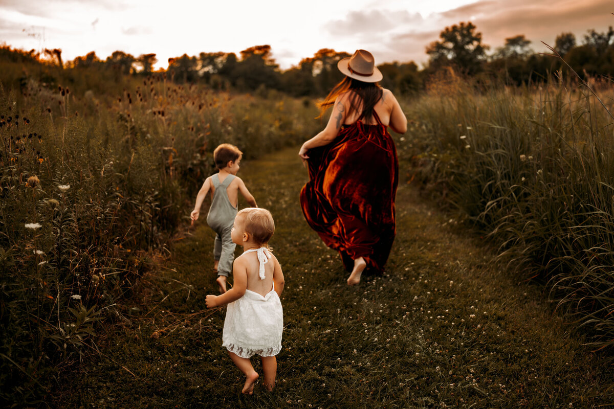 Mother and two children run freely down a grassy path surrounded by wildflowers