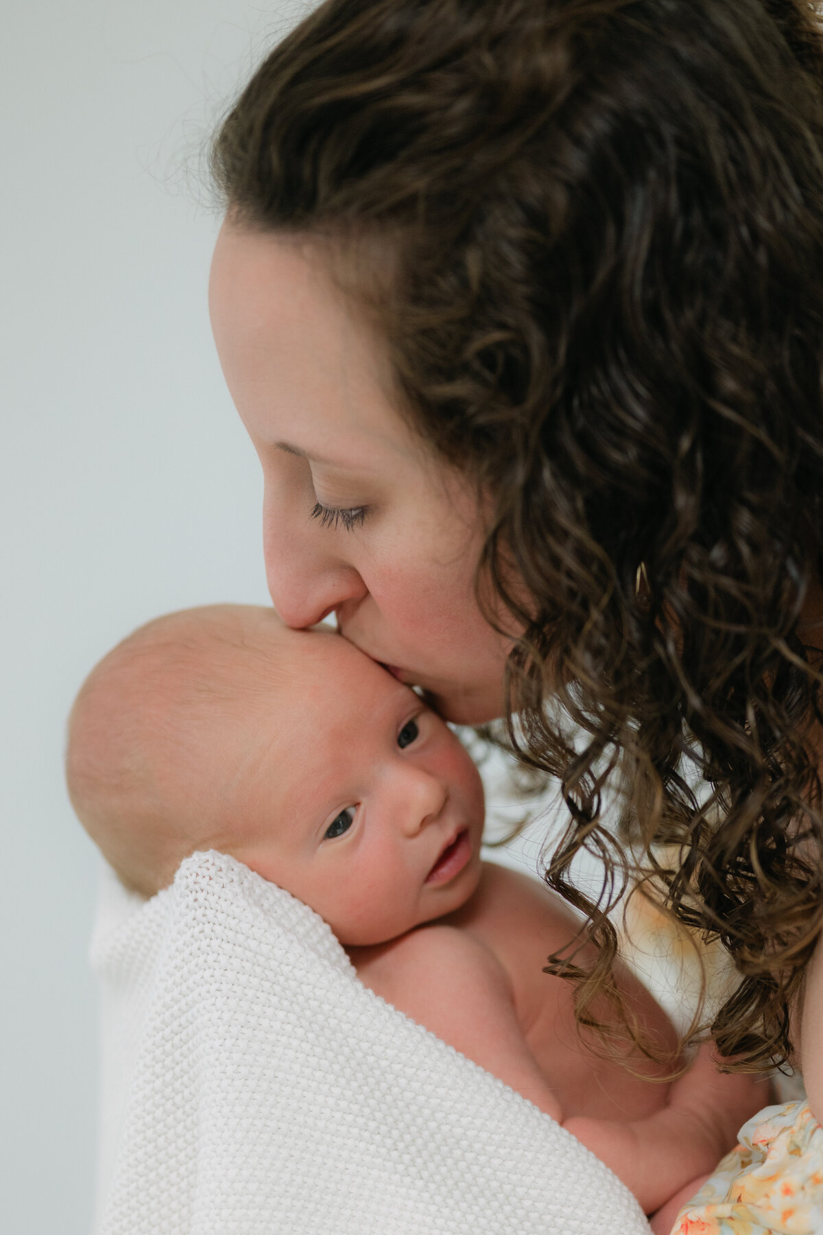 Newborn milestone photo of a mom kissing her baby in Bainbridge, capturing precious fleeting moments, serving Tallahassee area
