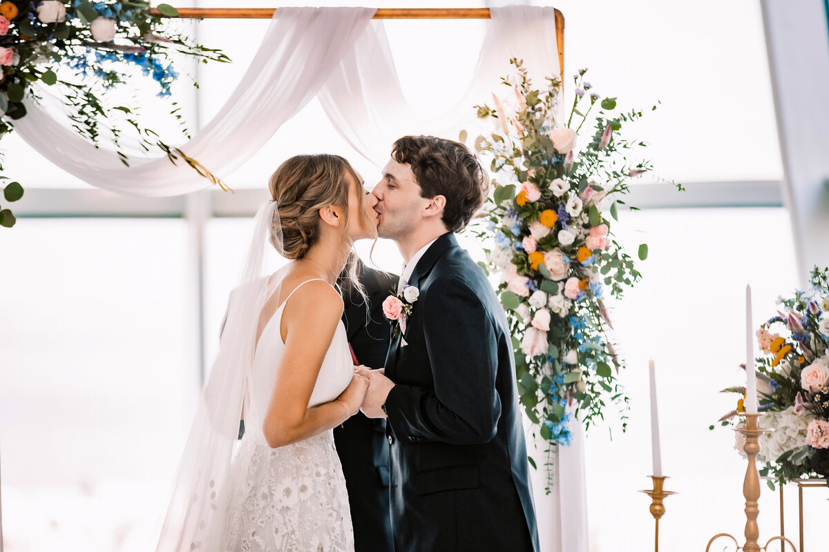 Newlyweds kiss under the arbor to end their indoor wedding ceremony