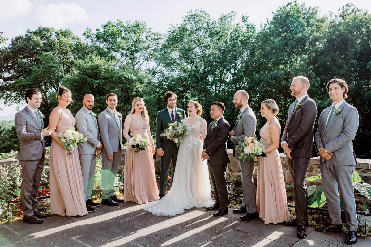 The bride and groom are standing together with their bridesmaids and groomsmen, with trees in the background.