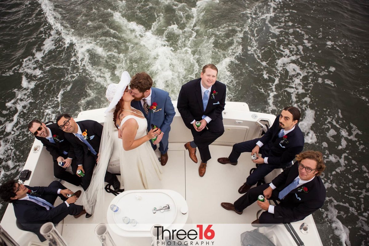 Newly married couple share a kiss on the back of the boat as the Groomsmen sit around and watch