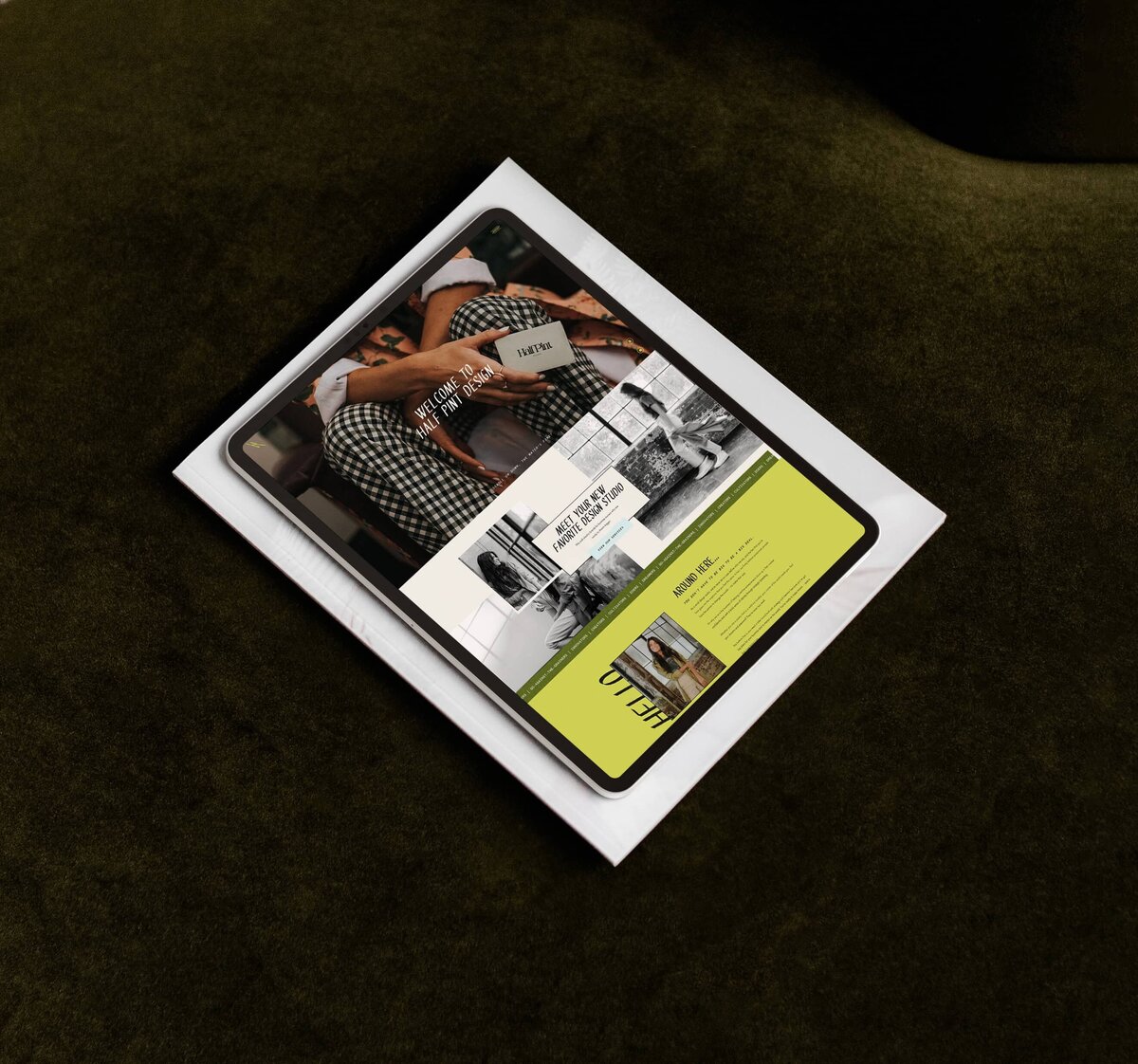 A tablet displaying a website layout with images and text, positioned at an angle on top of a sheet of white paper on a dark green fabric background, exemplifying the meticulous craftsmanship of a branding designer.