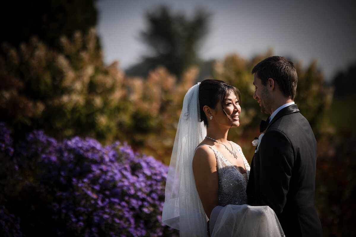 A couple poses in a garden with purple flowers at a destination wedding in Vermont