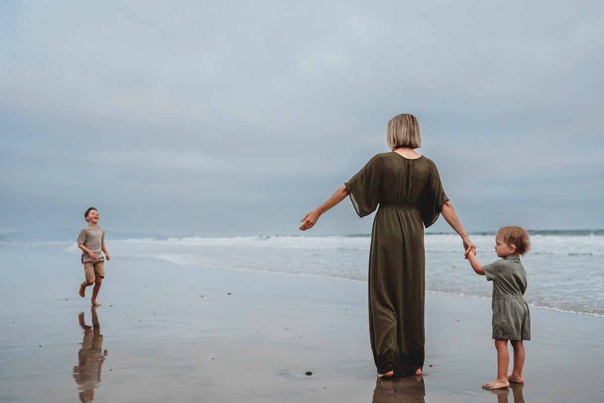 Mother holding hands with her children while standing at the edge of the ocean in Del Mar, San Diego family photography.