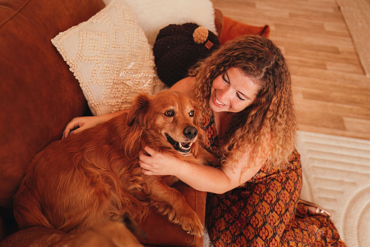 Baasje en hond vanop zetel al knuffelend tijdens een fotosessie in de daglichtstudio. 