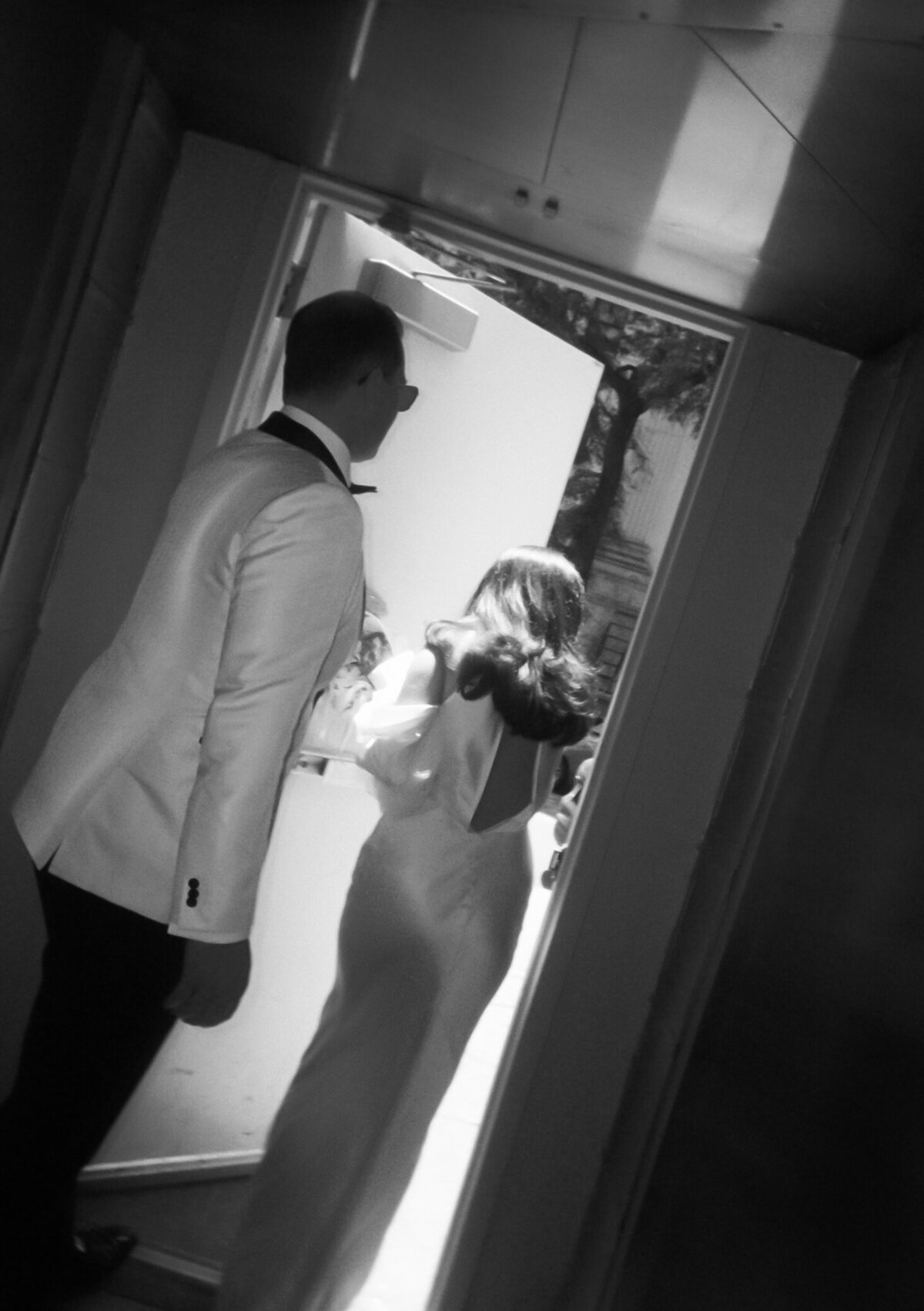 Bride and groom walk hand in hand out the doors of New York City Hall, captured in a timeless black and white photo.