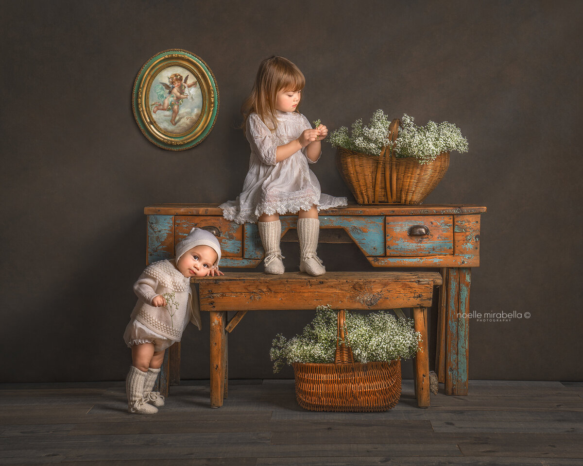 Children at antique table with baby's breath flowers. Antique cupid painting on the wall.