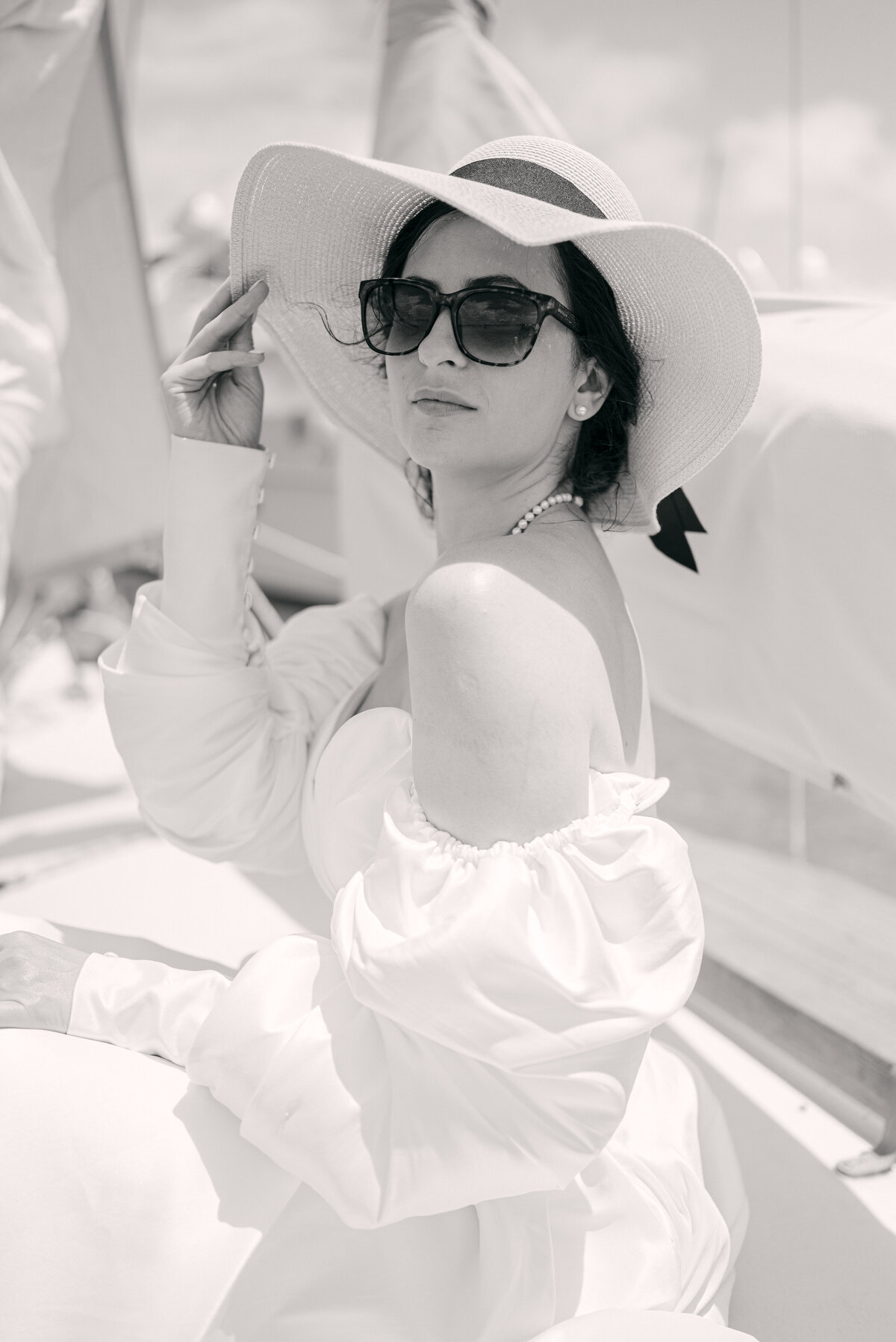 Bride holding sun hat and wearing sunglasses on a boat