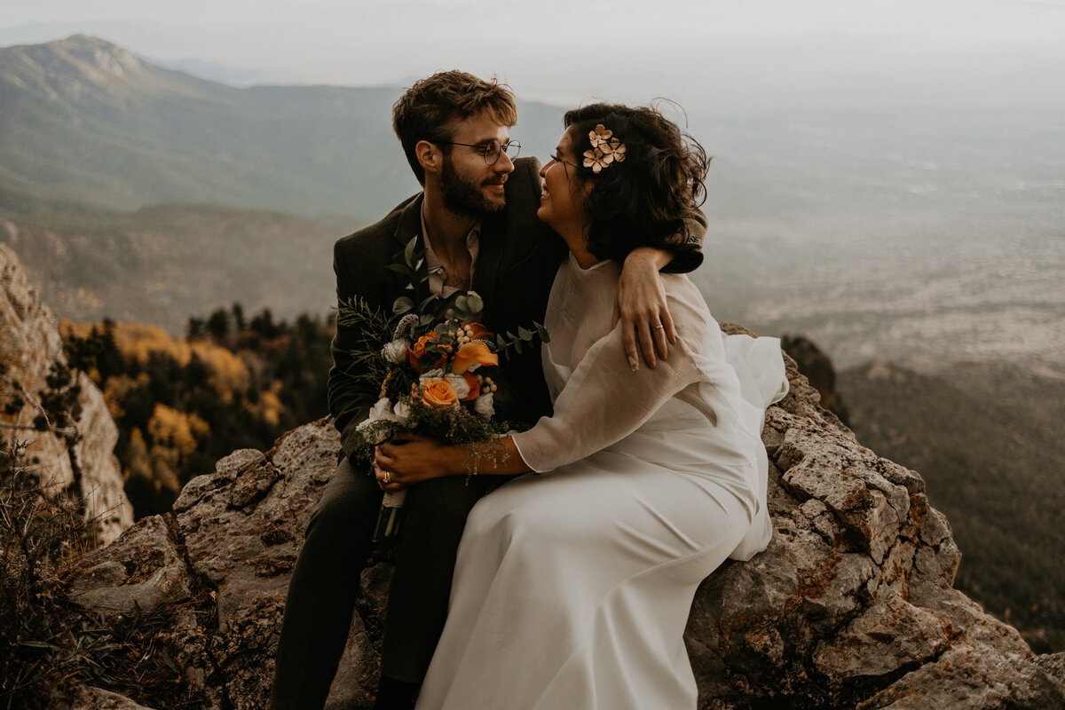 bride and groom sitting on the edge on the Sandia Mountain Peak with Albuquerque below them