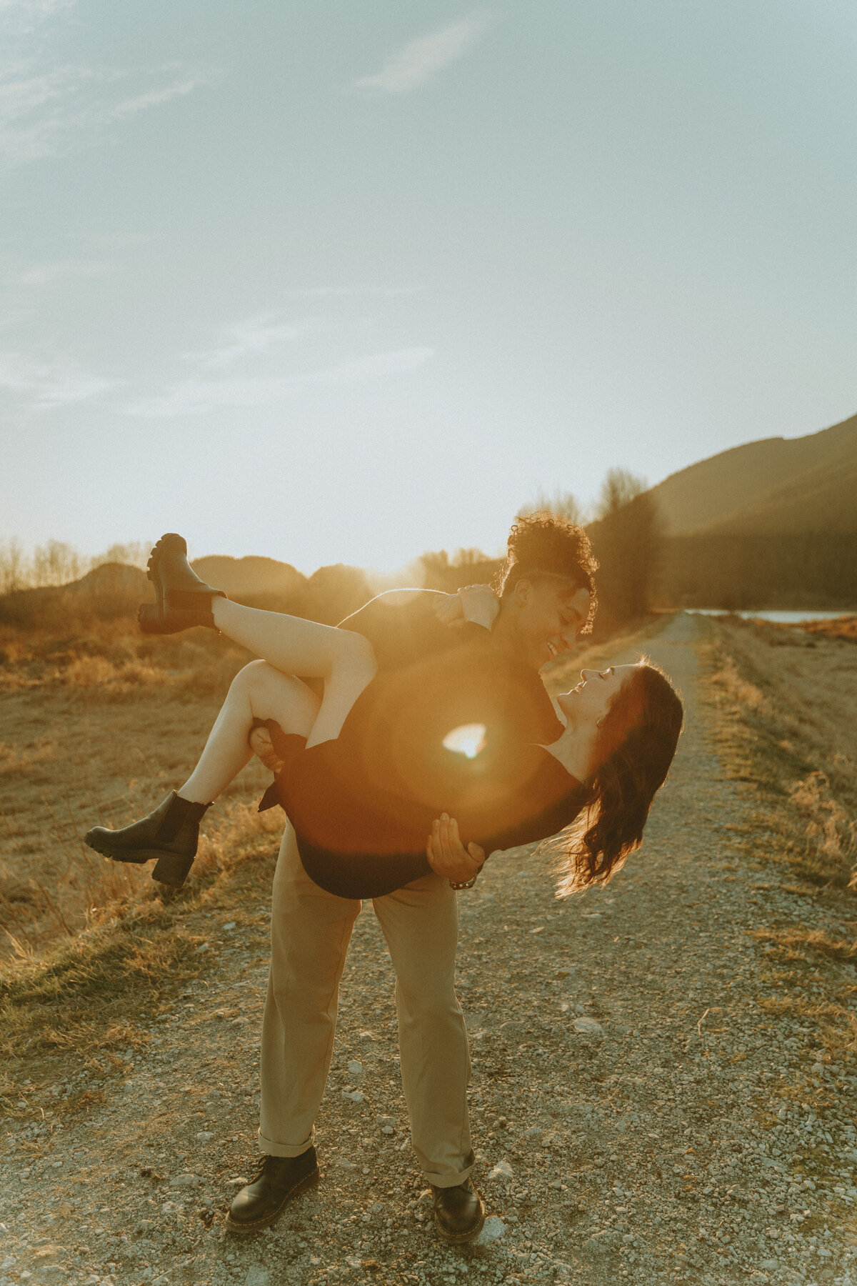 dreamy golden hour photo with sun flare of a guy carrying a girl dipping her about to kiss