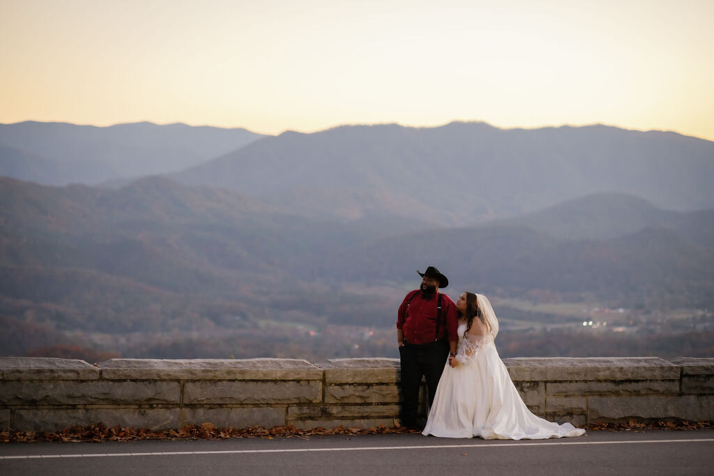 bride holding her grooms arm as he has his hands in his pockets and looks off to the mountains