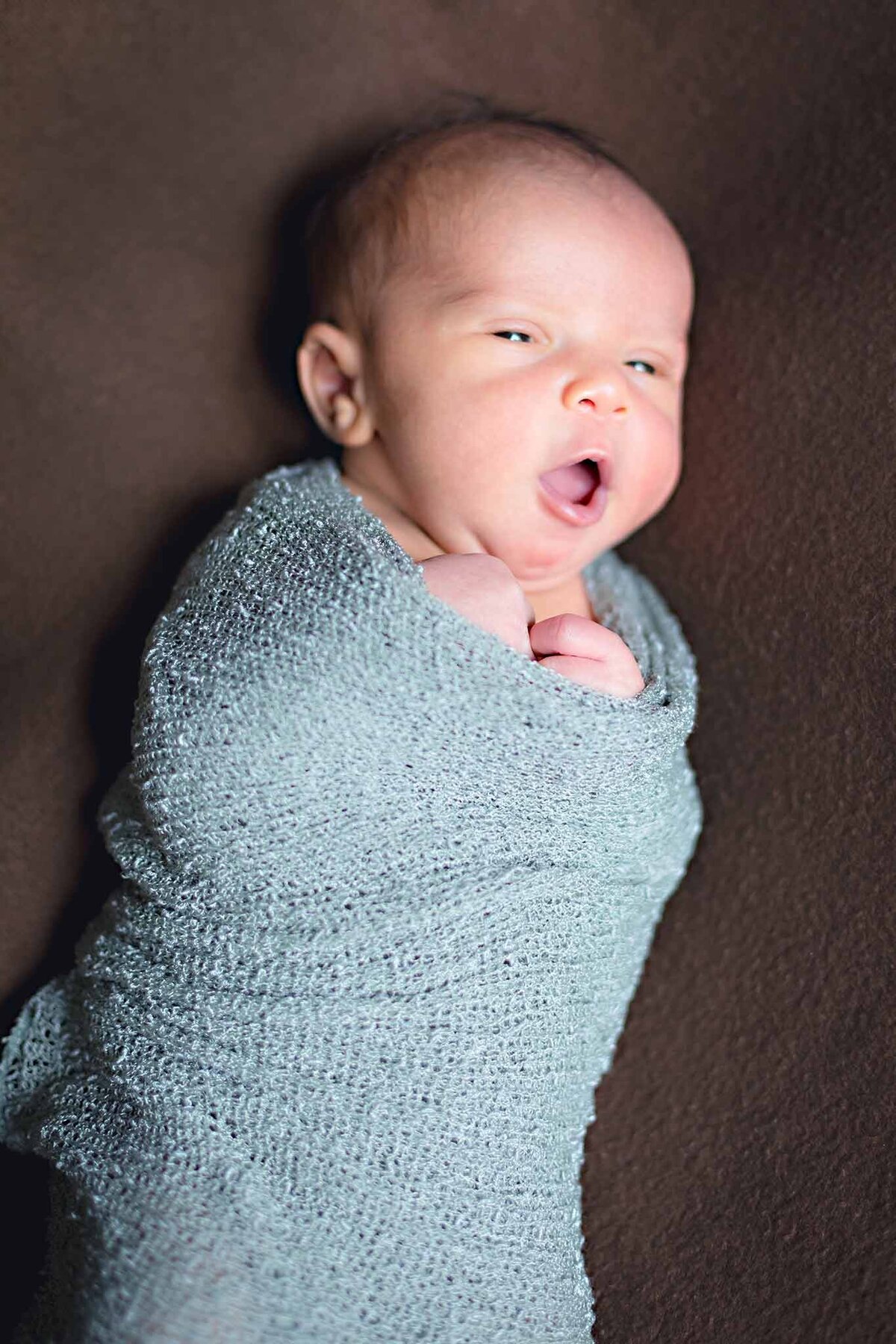 Newborn baby yawning while wrapped snuggly in a teal baby wrap in Columbia, SC