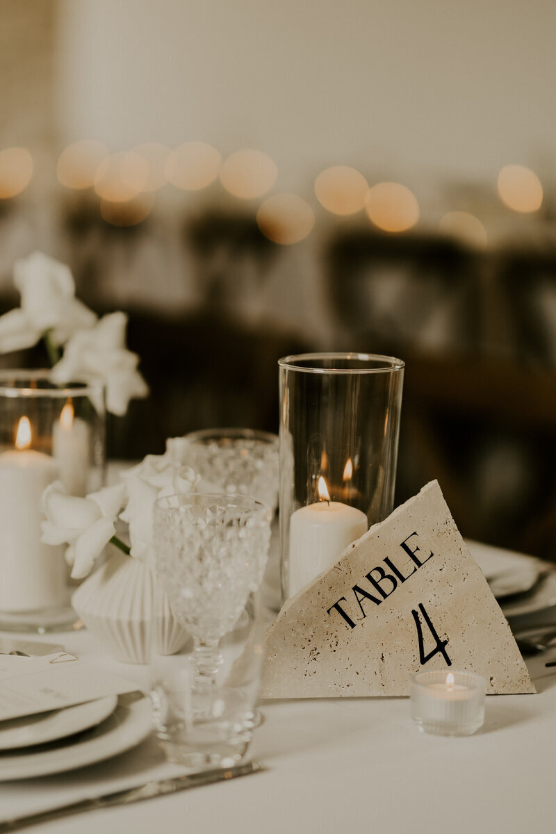 Décor indiquant "table 4" posé sur une table blanche agrémentée de vaisselle et de bougies. Photo prse par Laura, photographe de mariage en vendée.