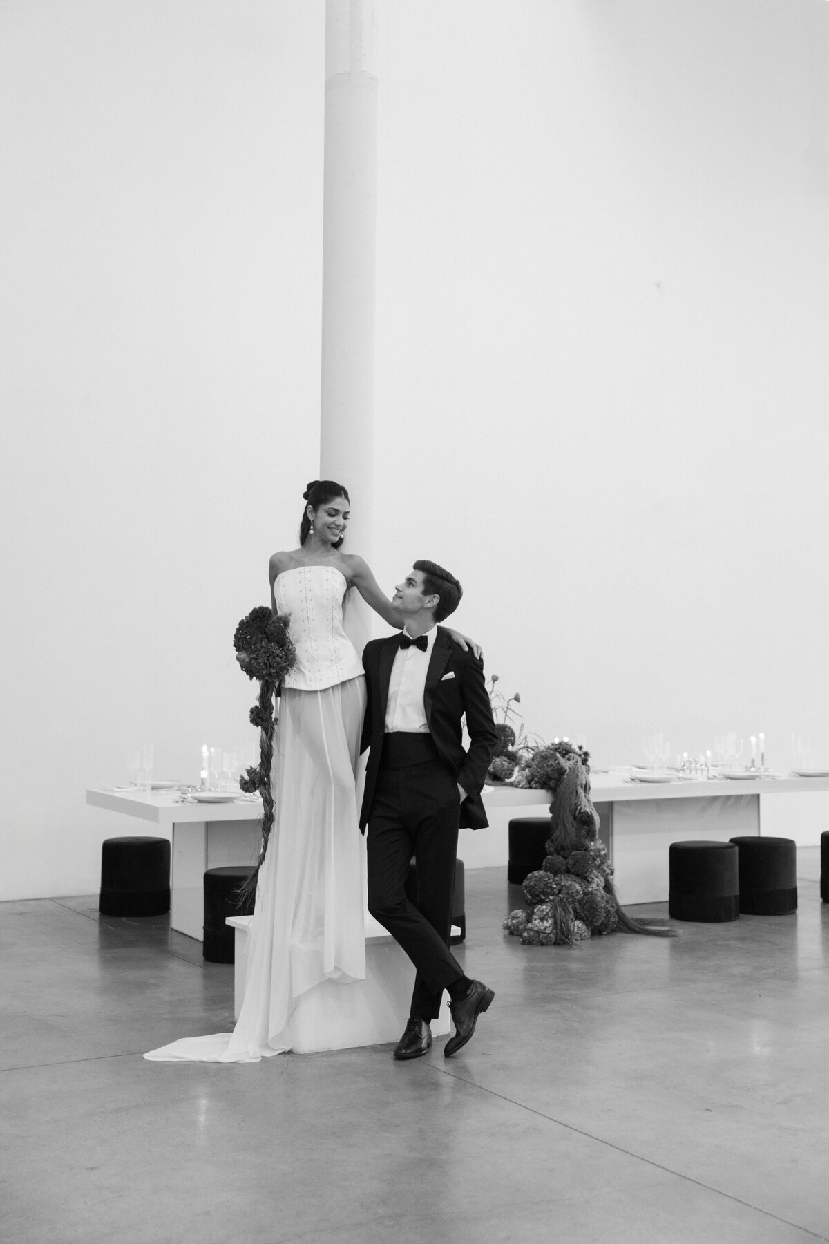 Bride seated with groom standing behind her, captured in a clean, minimalist ceremony setting with soft natural light.