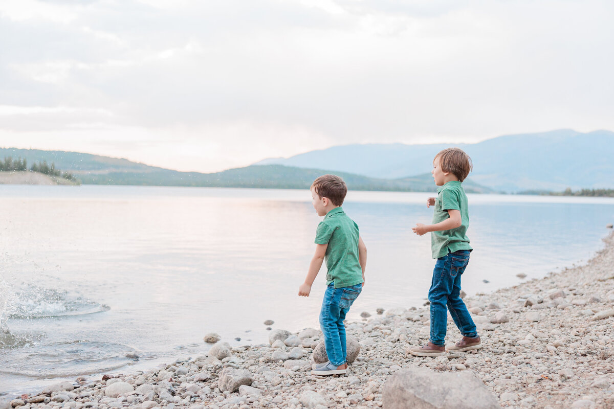 Two brothers are playing on the beach and throwing stones into the water of Lake Dillon on a summer evening captured by a Breckenridge Family Photographer