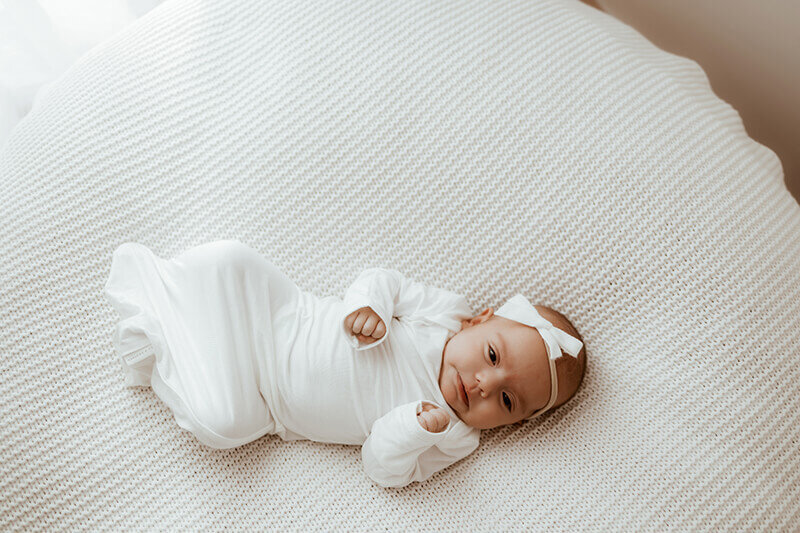 Newborn baby girl wearing a tight white sleeper sack during a denver newborn session