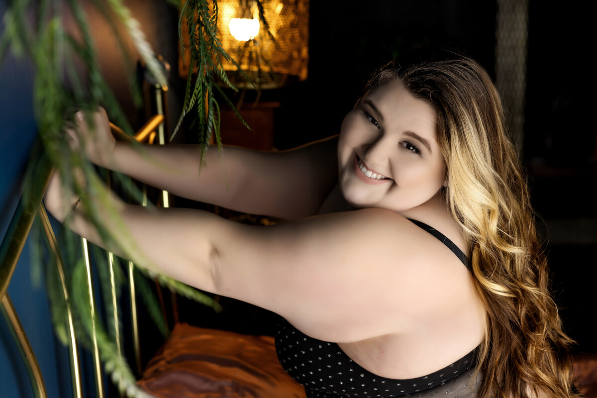 Smiling woman holding onto a headboard in an intimate boudoir portrait captured by Joclyn in Cedar Rapids, Iowa