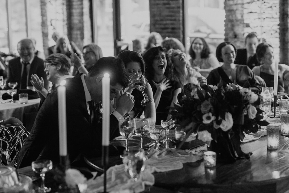 Black and white image of wedding party laughing during toasts