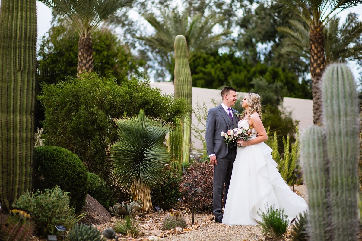 Bride and groom look at each other in a desert garden by wedding photographer PMA Photography.