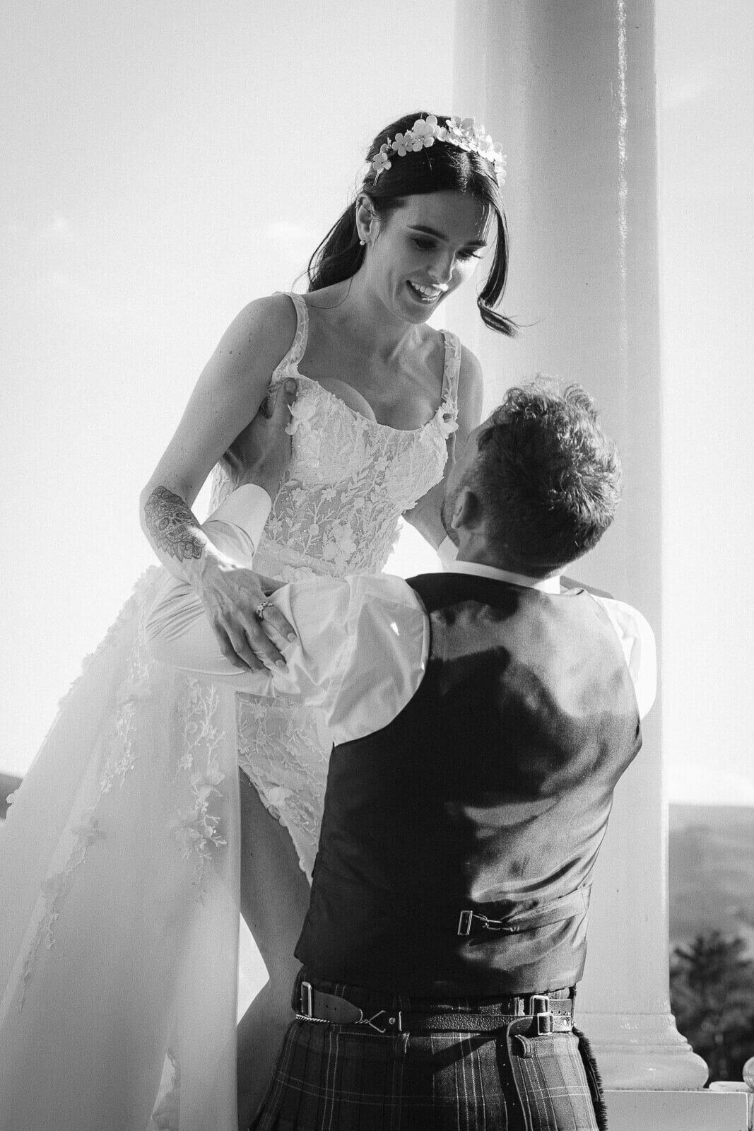 Groom lifts his bride up in jubilation. She towers above him and smiles.