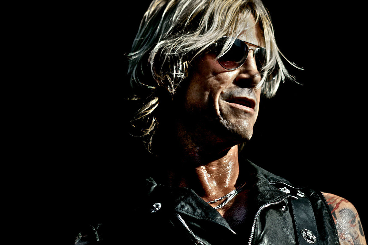 Duff McKagan musician portrait wearing black leather vest and sunglasses against black background