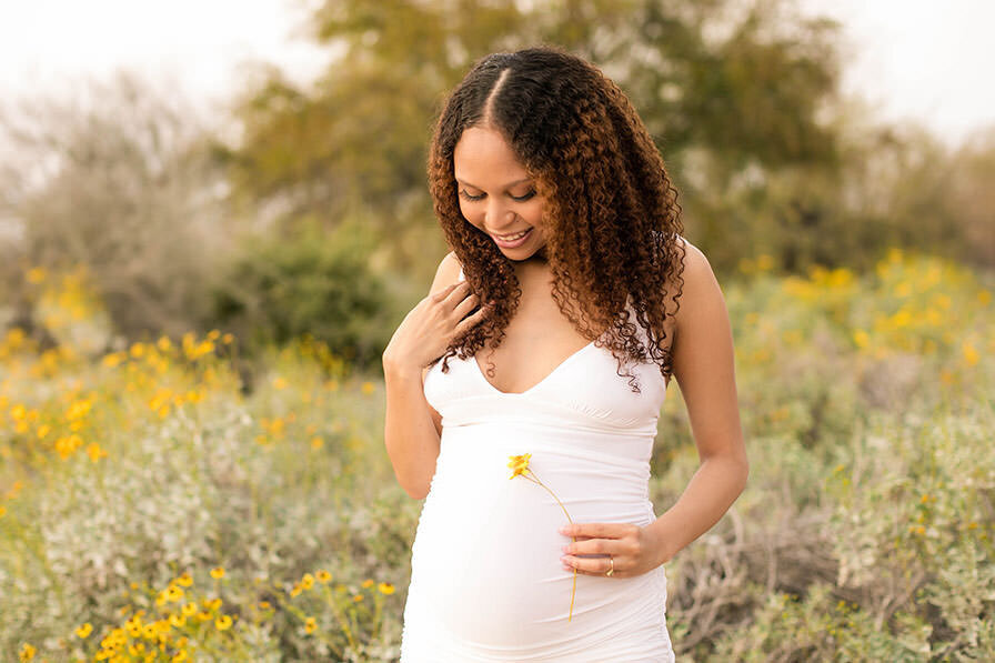 Pregnant woman in white dress in field of flowers at her outdoor maternity photo shoot