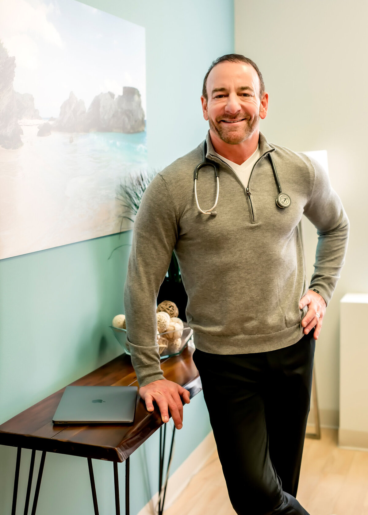 A male doctor standing in his office wearing a stethoscope, posing for a South Shore MA branding photographer.