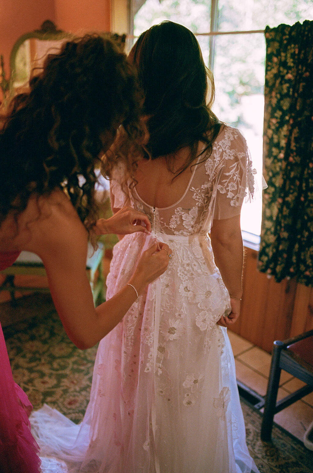 A bride getting her dress tied, representing the little moments she and her bridal party enjoy together.