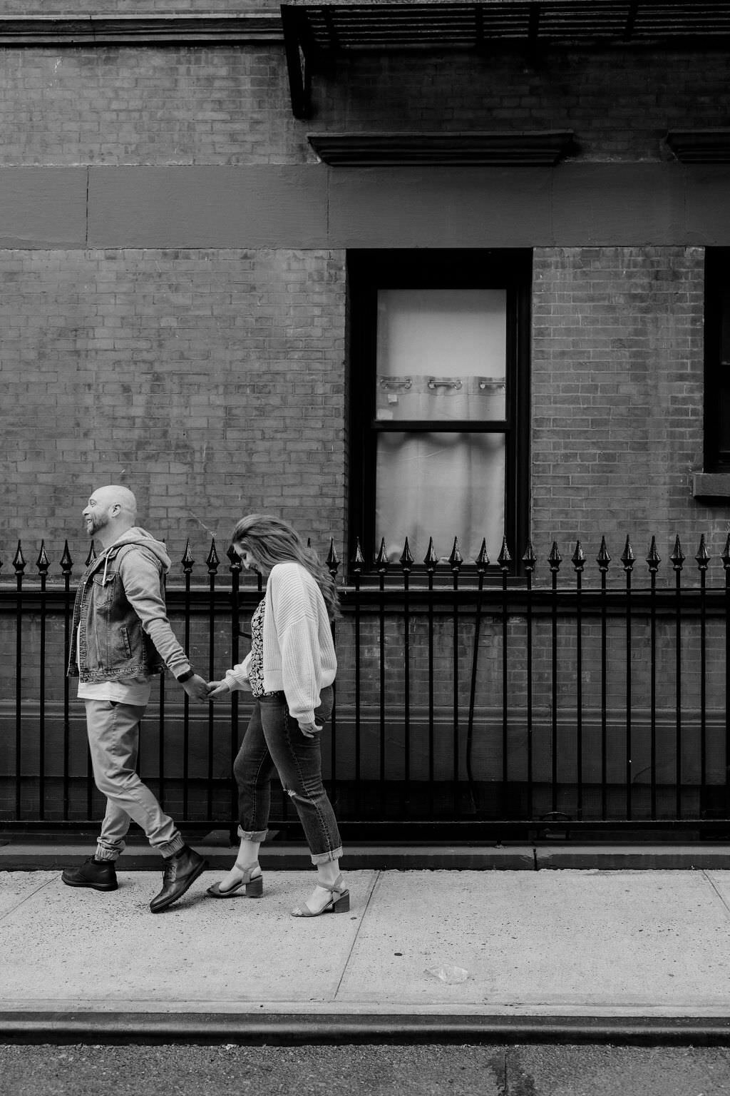 black and white photo of a man leading a woman down a sidewalk as they hold hands