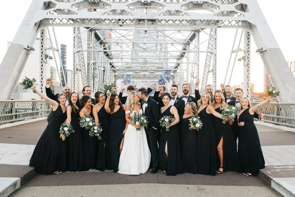 Nashville pedestrian bridge bridal party in all black and white carry greenery and white bouquets
