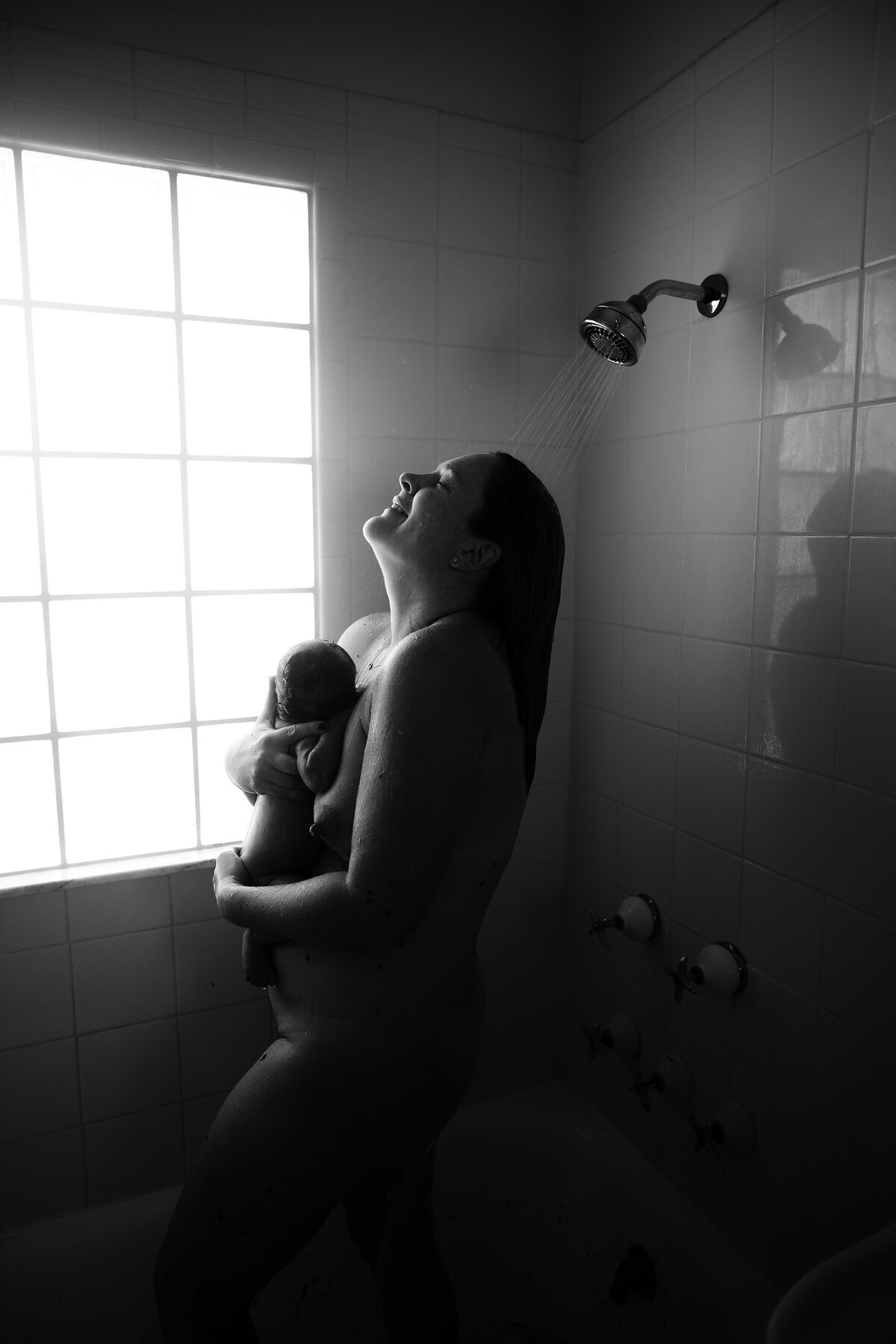 a mom holding her newborn baby in the shower during a at home documentary photo shoot
