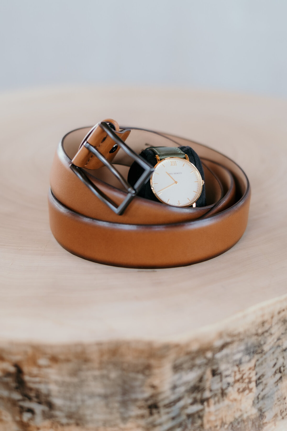 Der Gürtel des Bräutigams liegt eingerollt auf einem Holzstamm. In der Mitte liegt seine Uhr.