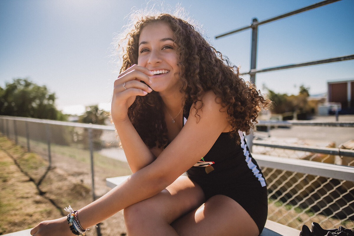 Olivia smiles and sits on bleachers for headshots taken by Los Angeles photographer.
