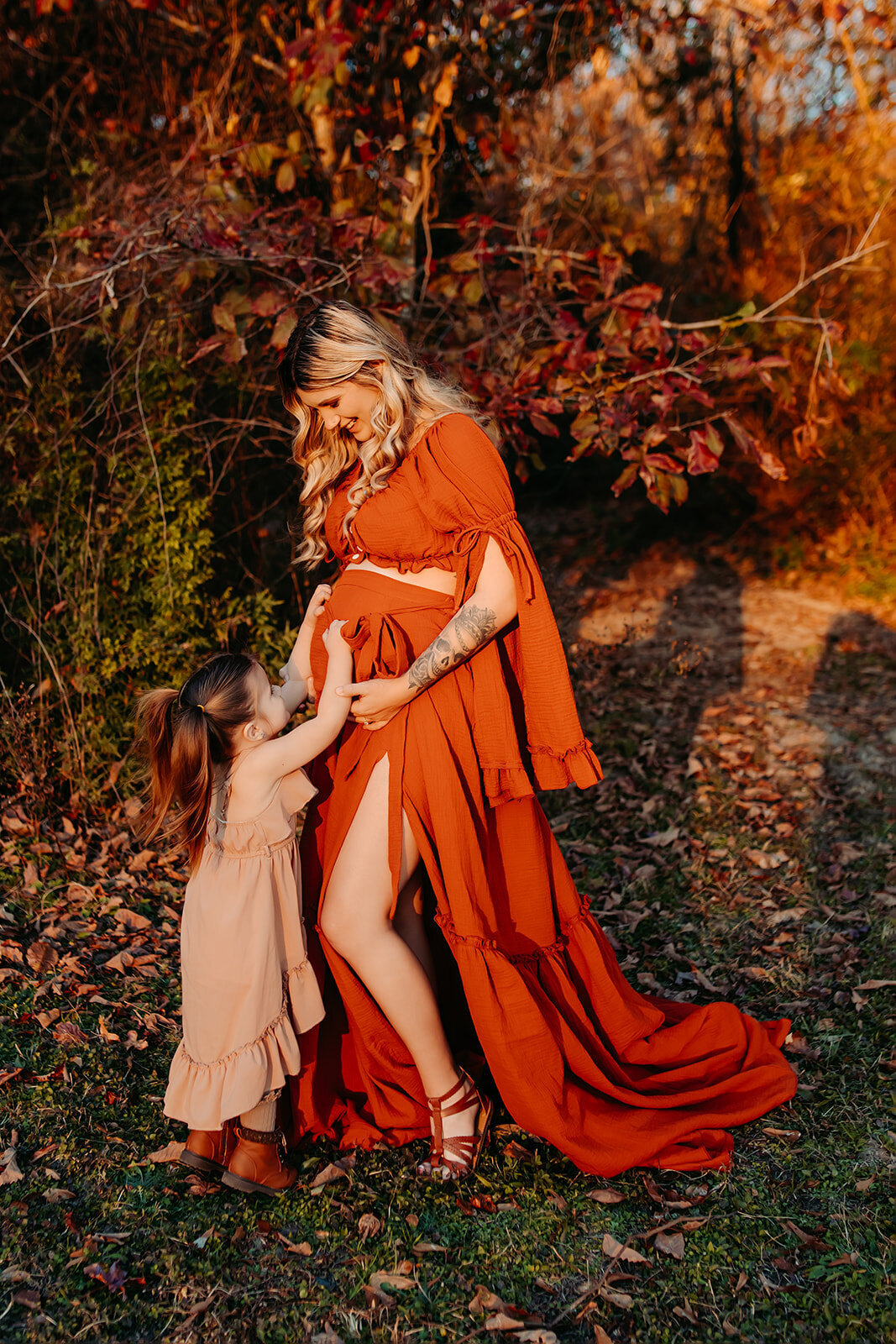 Kingwood TX maternity photography – expecting mother in burnt orange gown holding baby bump, outdoor golden-hour portrait