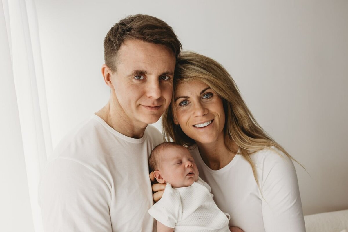 Family portrait in Wijchen, Gelderland, featuring a proud mother and father looking at the camera while cradling their precious sleeping newborn baby