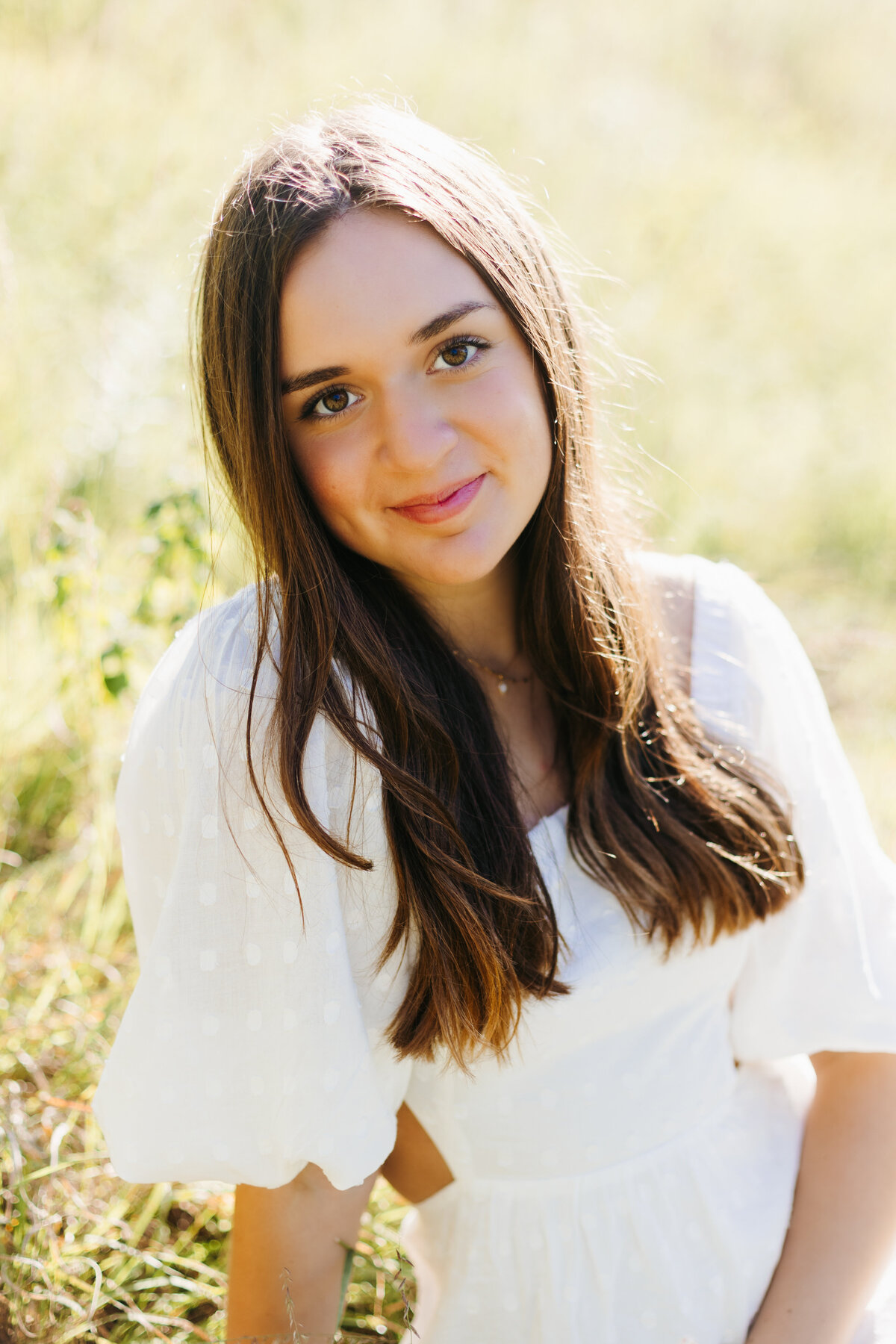 Close up portrait of Senior girl in a white dress in a grassy field