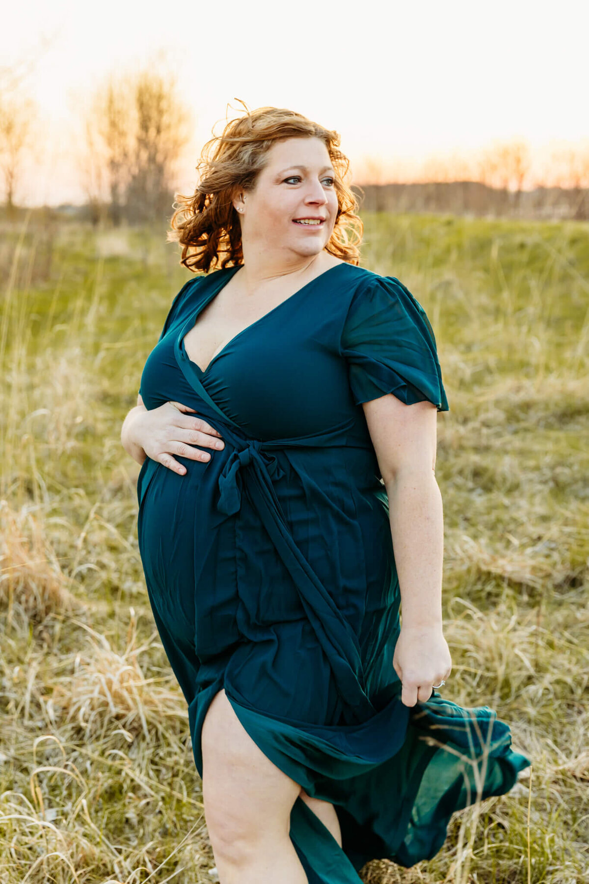 gorgeous mom to be walking through a field as the wind blows her hair and dress