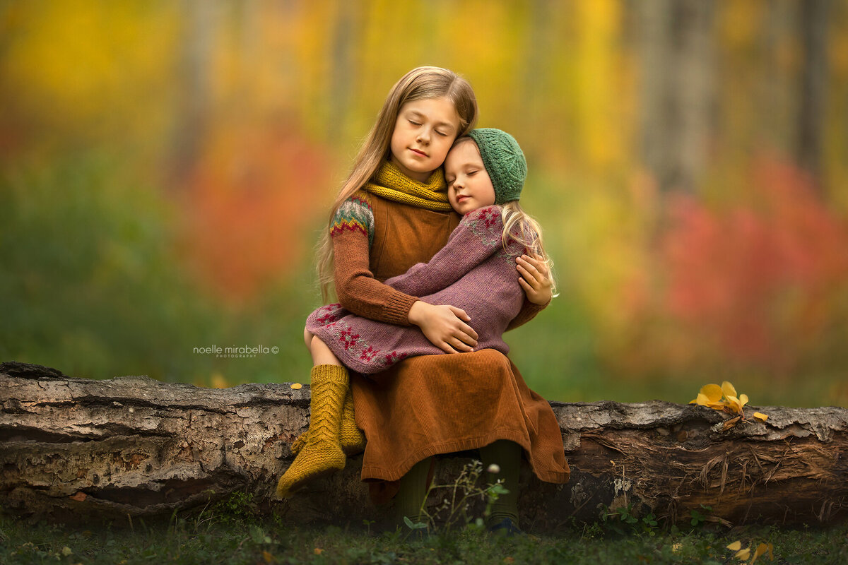 Girls hugging on a wooden log in autumn outdoors.