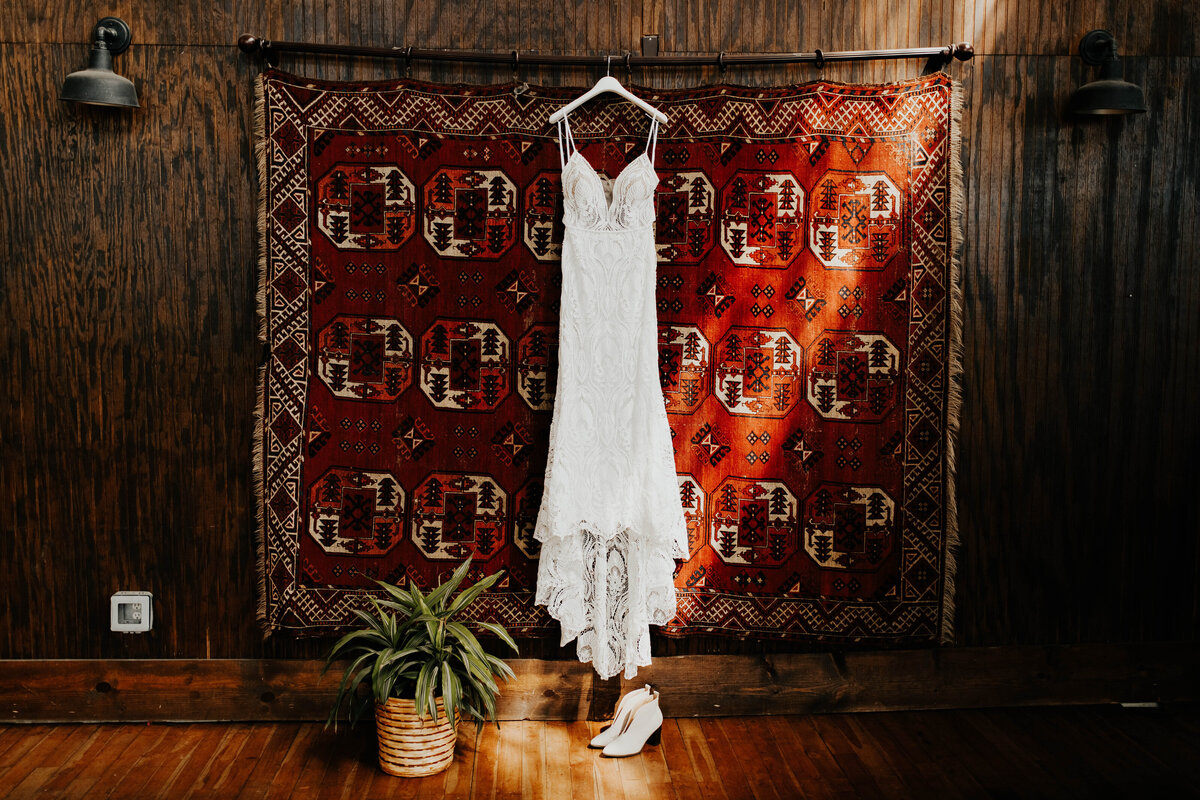 White wedding dress hanging up with boho rug as backdrop
