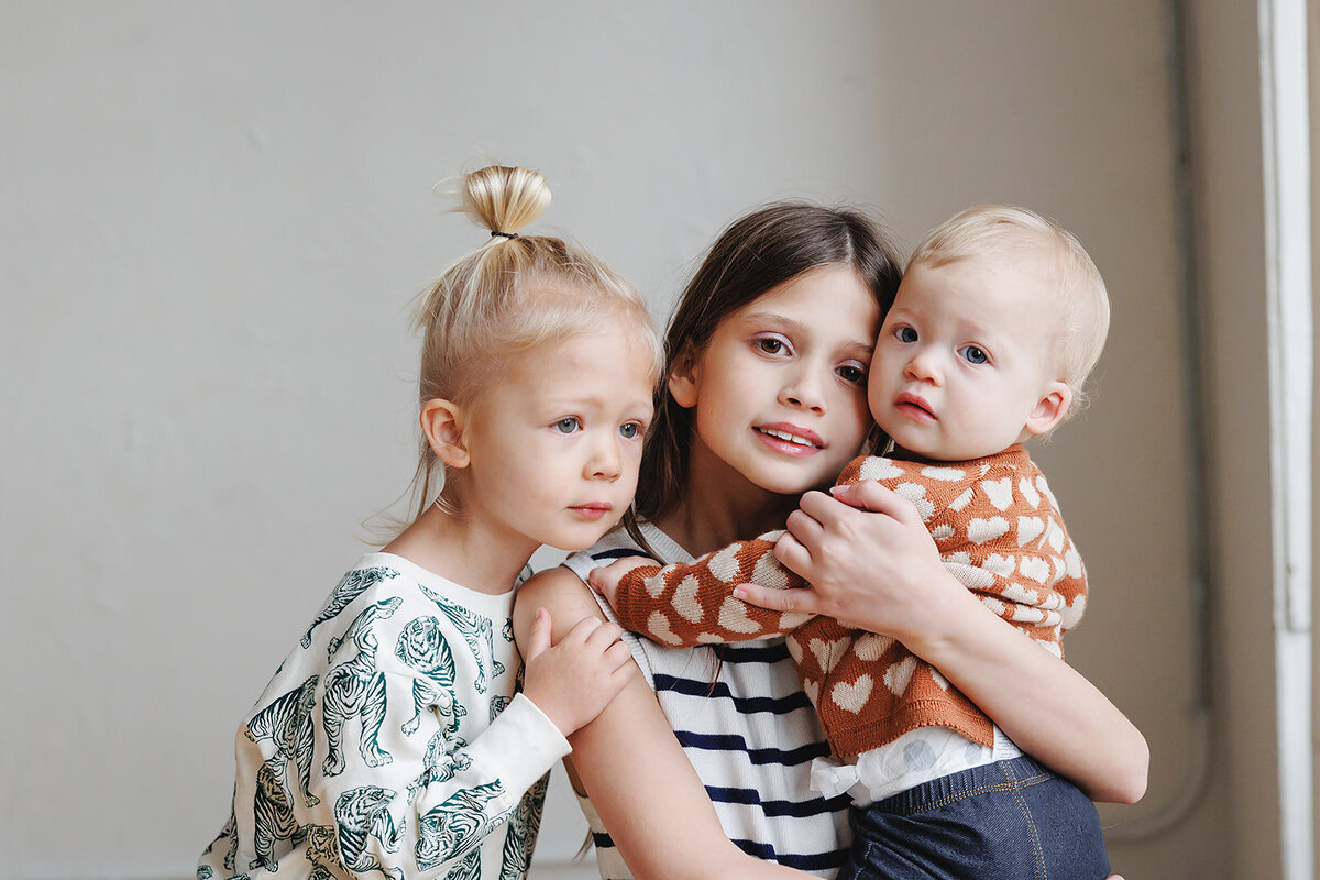 Portrait of three children posed in front of a taupe backdrop