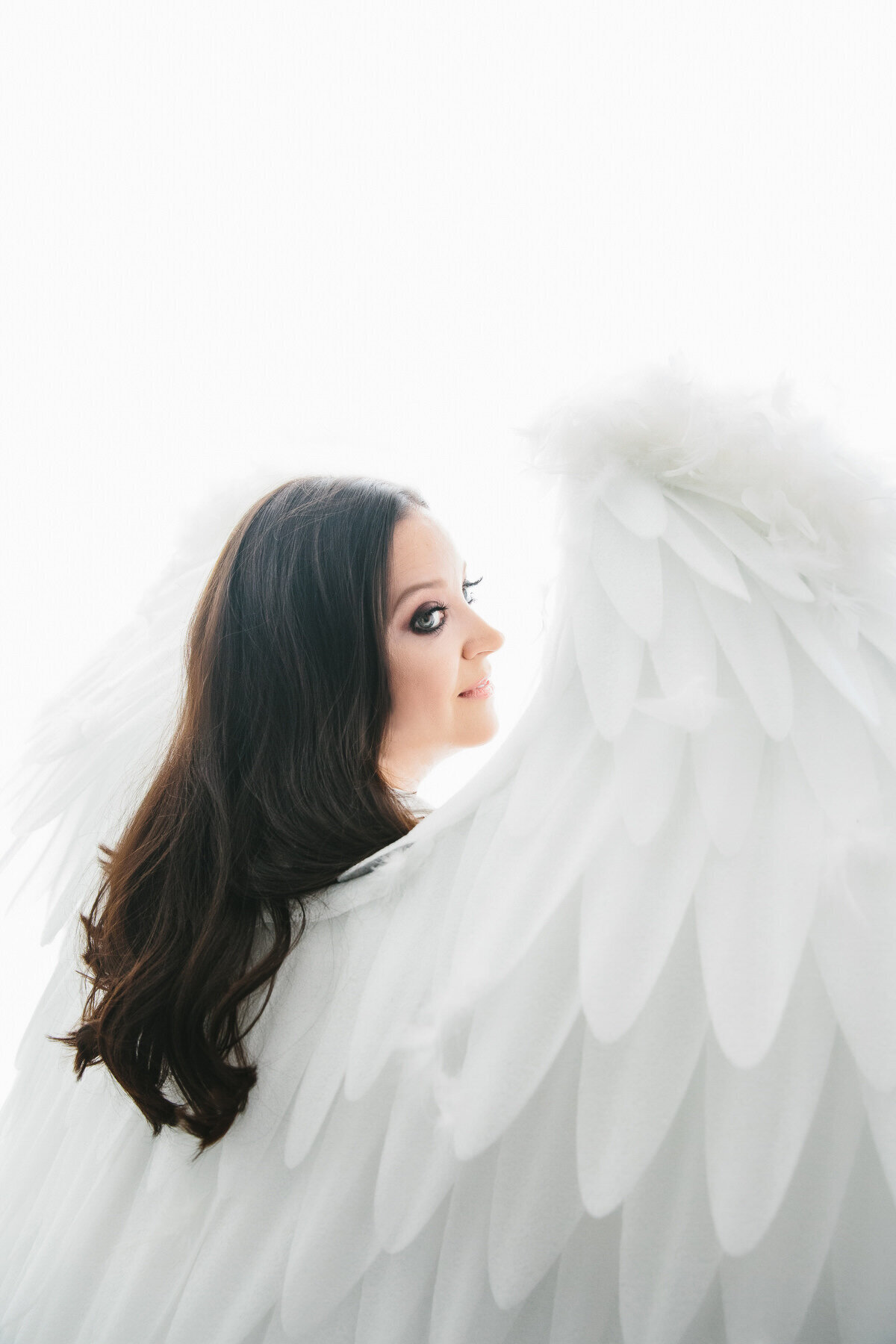 Light and airy portrait of brunette woman looking over shoulder of angel wing