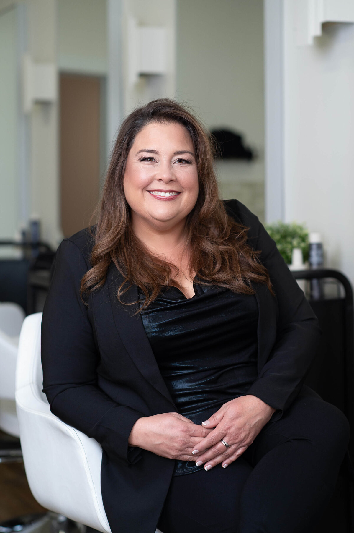 a stylist with long dark hair and black clothing sitting in a white salon chair.  Captured on-location at Richardson Hair Design by Ottawa branding photographer JEMMAN Photography