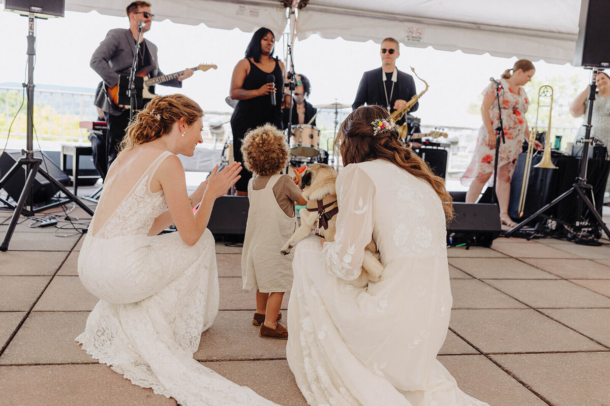 Brides kneeling down with child looking at band at Cornell University wedding