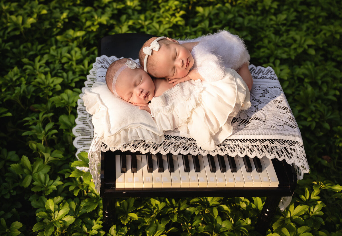 Baby twins asleep on eachother on a small piano out side in a garden of greens near Grimsby, Ontario.