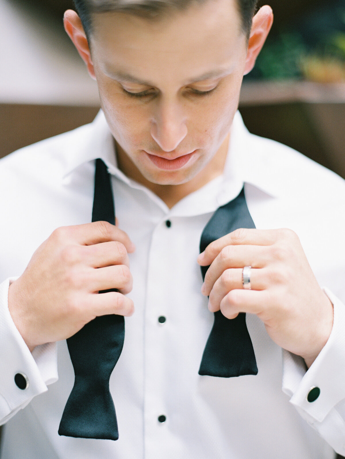 Groom ties his black bowtie on his wedding day