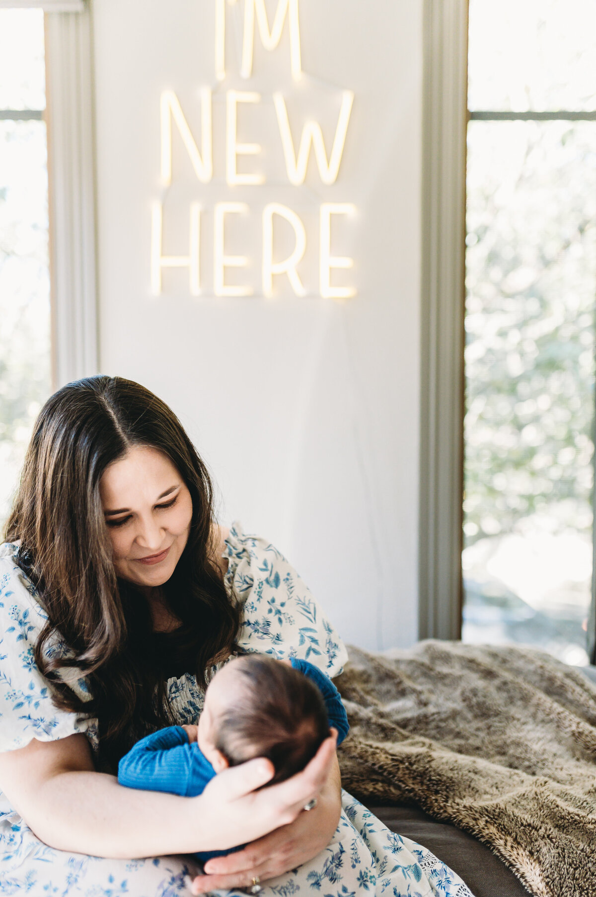 mother holding newborn baby boy at home under a sign that says i'm new here