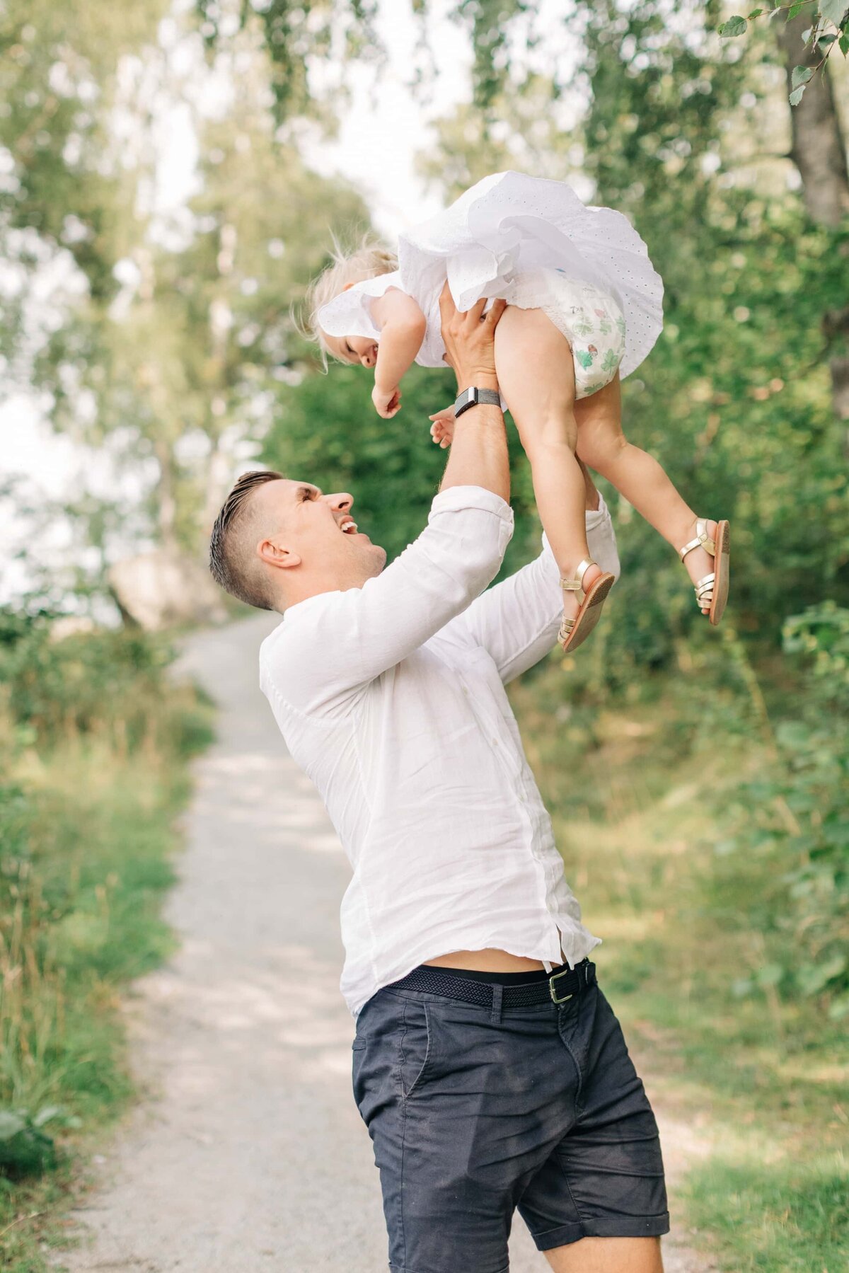 Pappa som lyfter upp sin dotter i luften på en grusgång