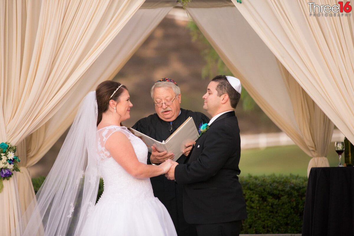 Rabbi performs a Jewish wedding while the Bride and Groom hold hands and face each other